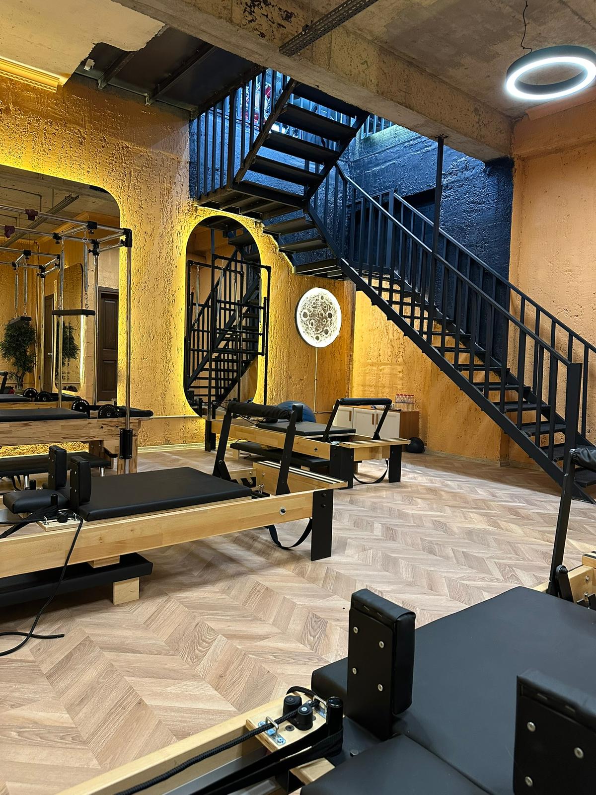 Reformer pilates salonu: ahşap zemin, altın duvar aydınlatması ve reformer yatakları